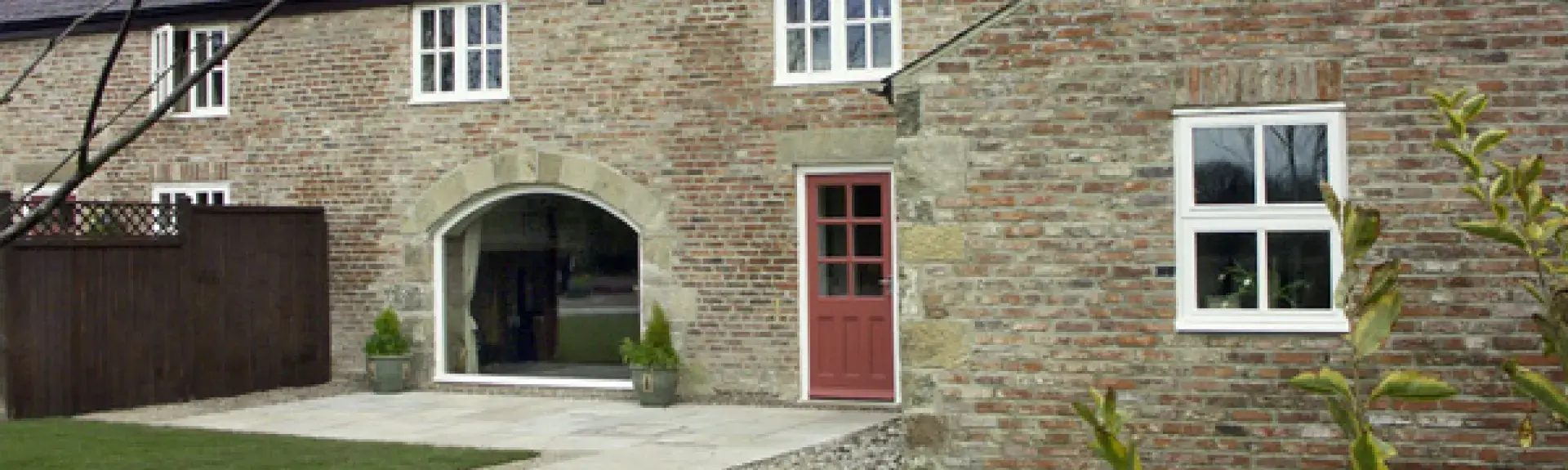 Two-lawns and a path ead to a stone-built terraced cotage with a foor-to-ceiling wide front window.
