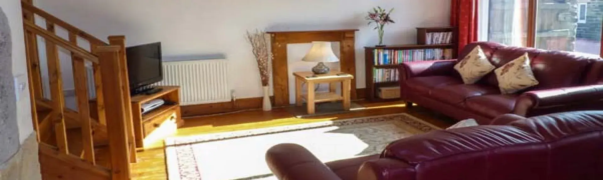 Interior of a spacious pine-floored lounge with pine beams, rugs and large sofas.
