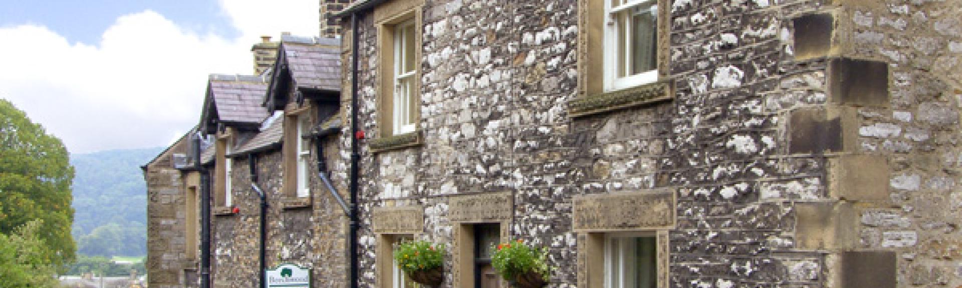 a double-fronted, stone-built terraced cottage on an empty street.