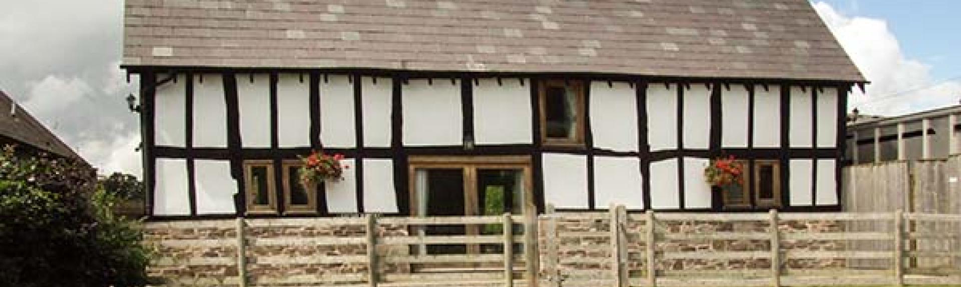 A historic 'black-white white' timbered farmhouse sits behind aterraced and fenced-in lawn.