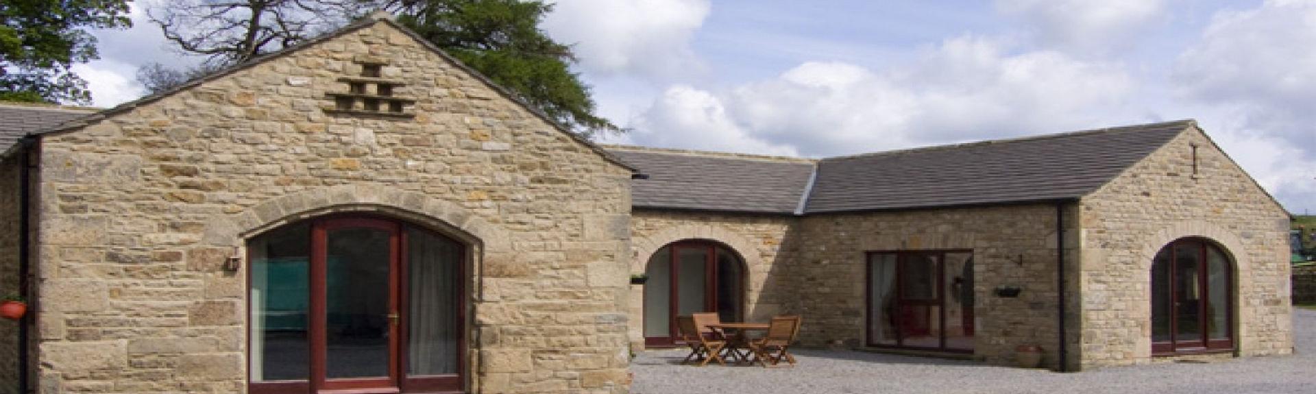 A U-shaped, stone barn conversion with floor-to-ceeiing windows looks out over a large shingled courtyard.