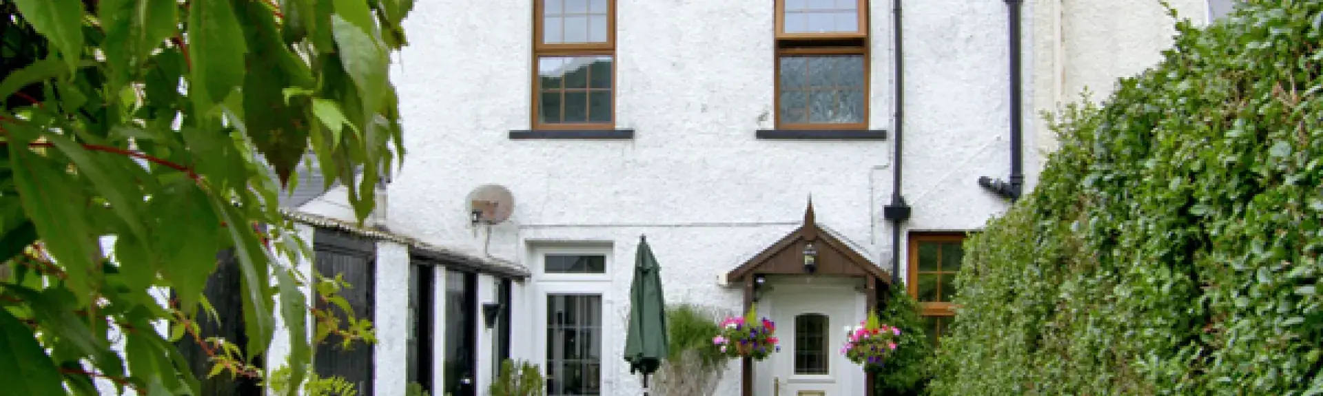 A 2-storey, stone-built gwynedd holiday covvage oveerlooks a garden full of poptted plants and shrubs.