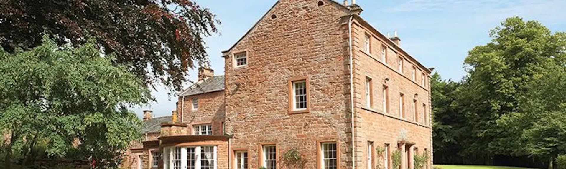 A Large 3-storey Country House surrounded by lawns and woodland.