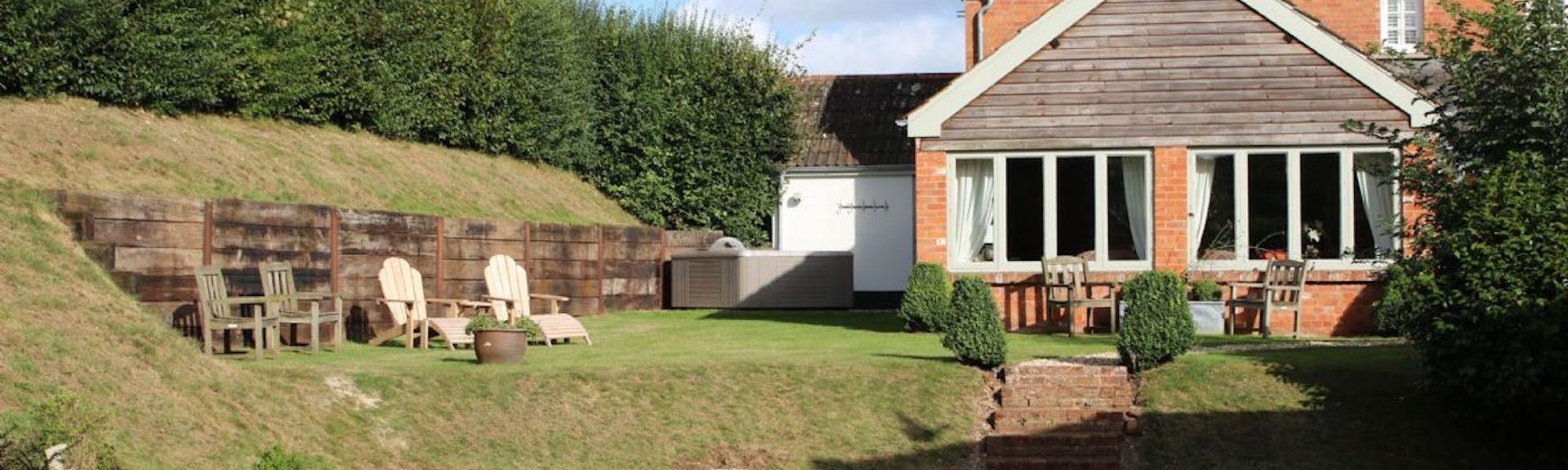 A two storey brick house with a large gable end overlooks a lawn and spacious parking area.