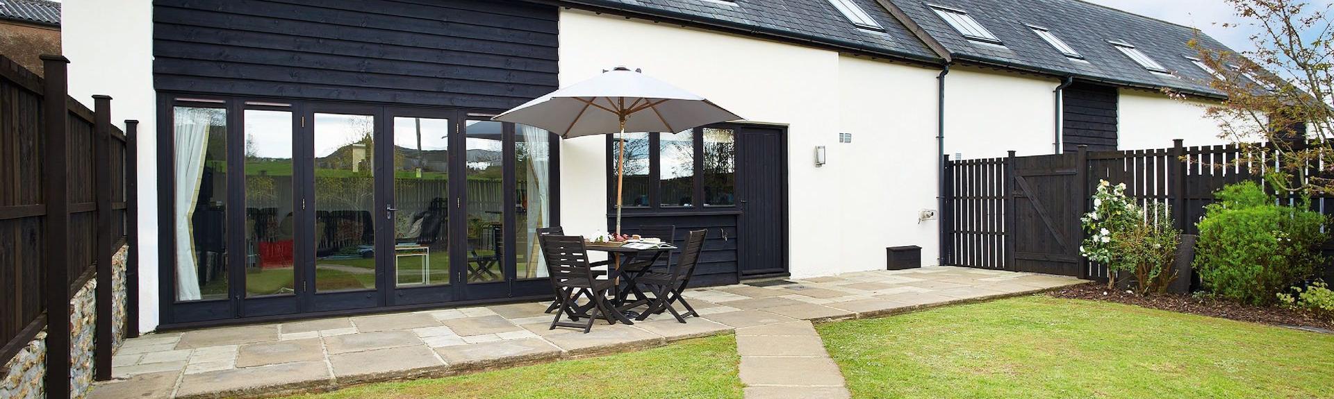 A semi detached, part-tiimbeer contemporary cottage with fold-back French windows, a patio and spacious lawn.