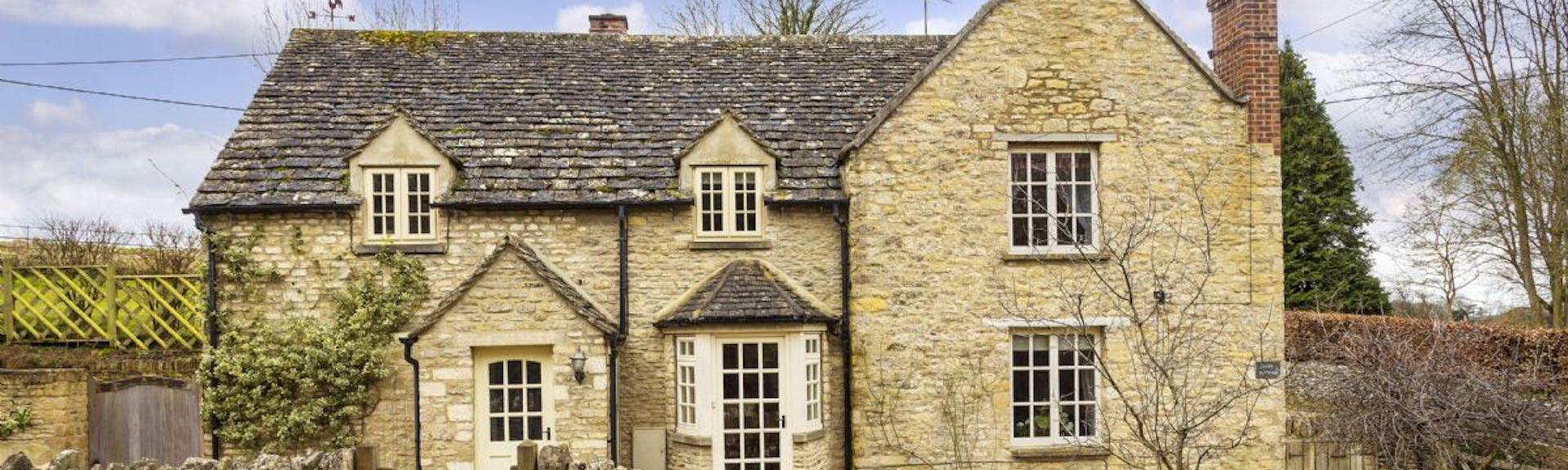 Cotswold cottage exterior with a bay window and low stone garden wall.