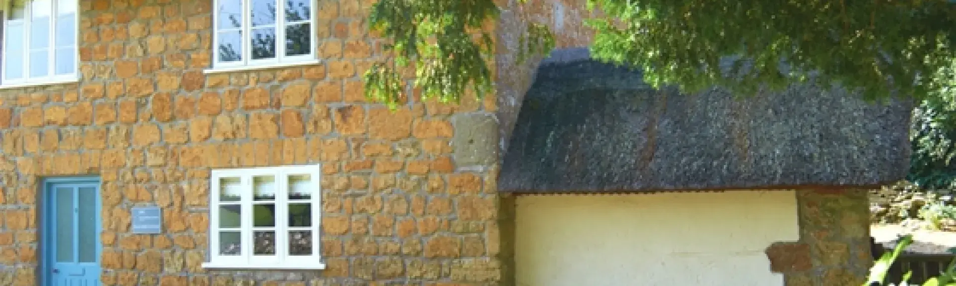 A honey-stone, thatched country cottage with a walled front garden.