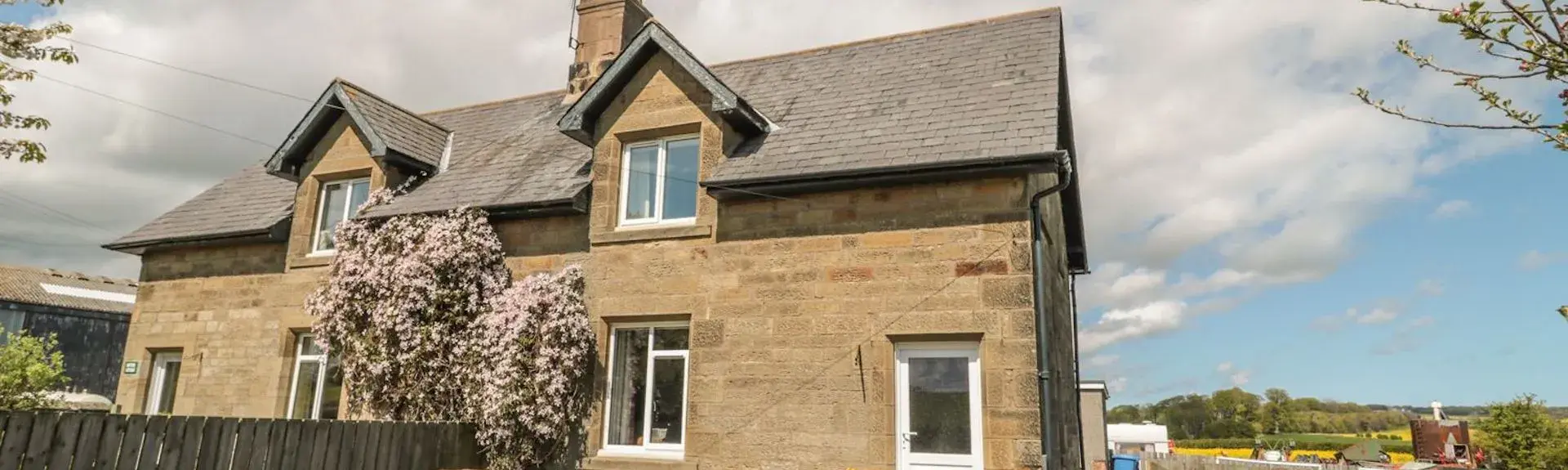 A semi-detached stone farm cottage with a lawn and picnic table.