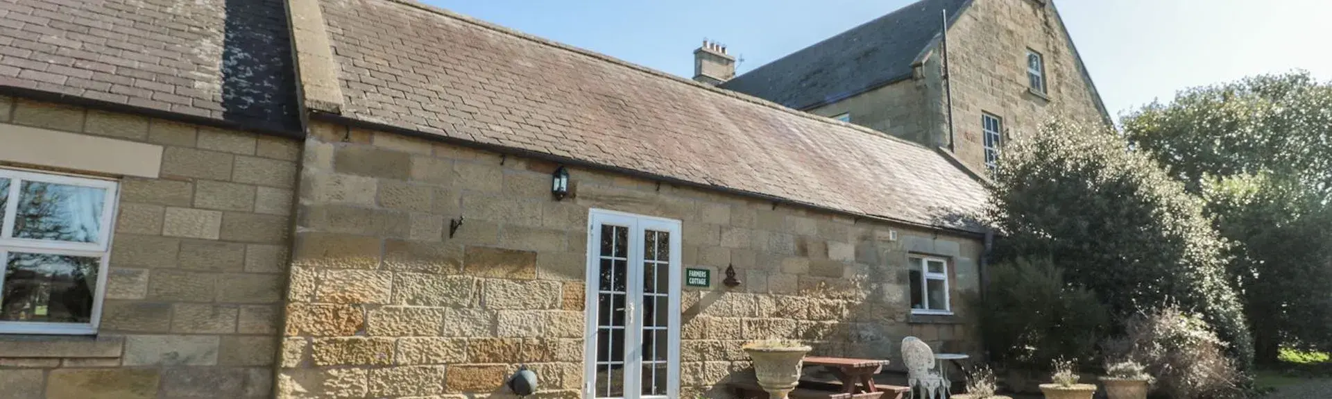 A siingle-storey stone-built cottage with French windows opening onto a paved courtyard.