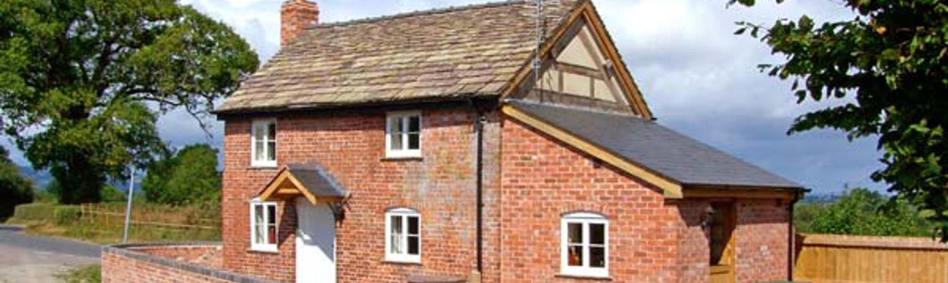 A red brick Herefordshire holiday cottage with a ground floor extension is surrounded by a low tone wall