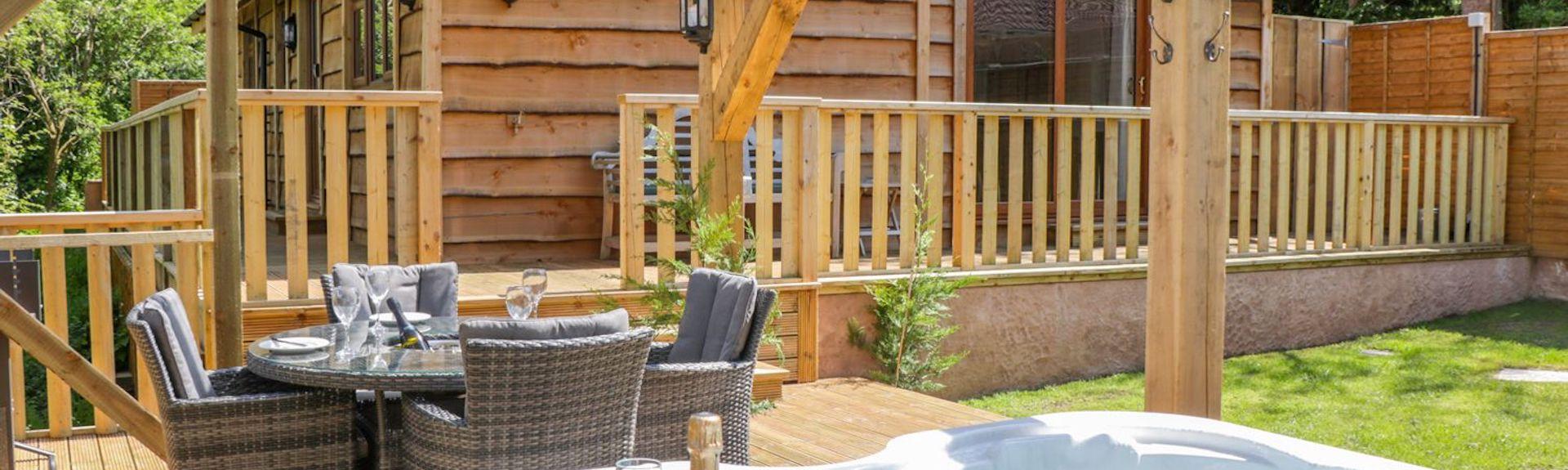A wooden holiday lodge in Washford overlooks a patio with a hot tub. on a terrace/