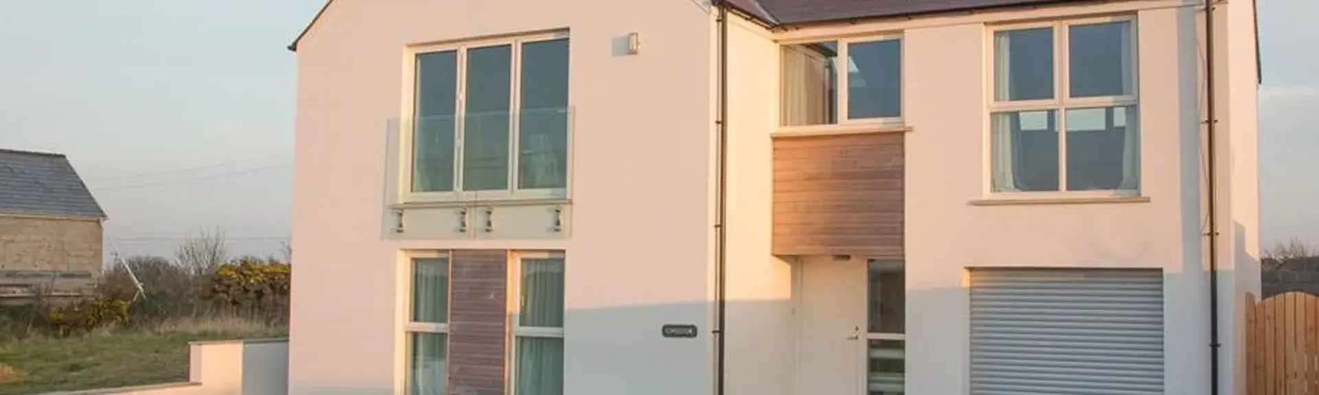 A modern detached house with large windows and space for off-road parking in front.
