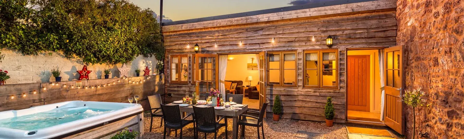 A wood-clad, single-storey Quantock Hills holiday home overlooks a courtyard with a hot tub at dusk.