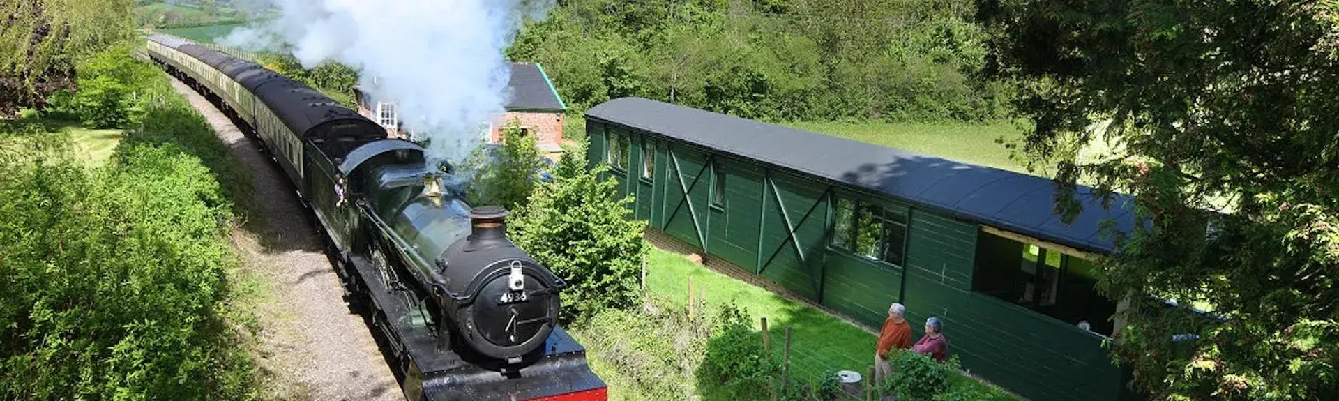 A stem engines rushes through Somerset countryside past two old carriages converted to holiday homes