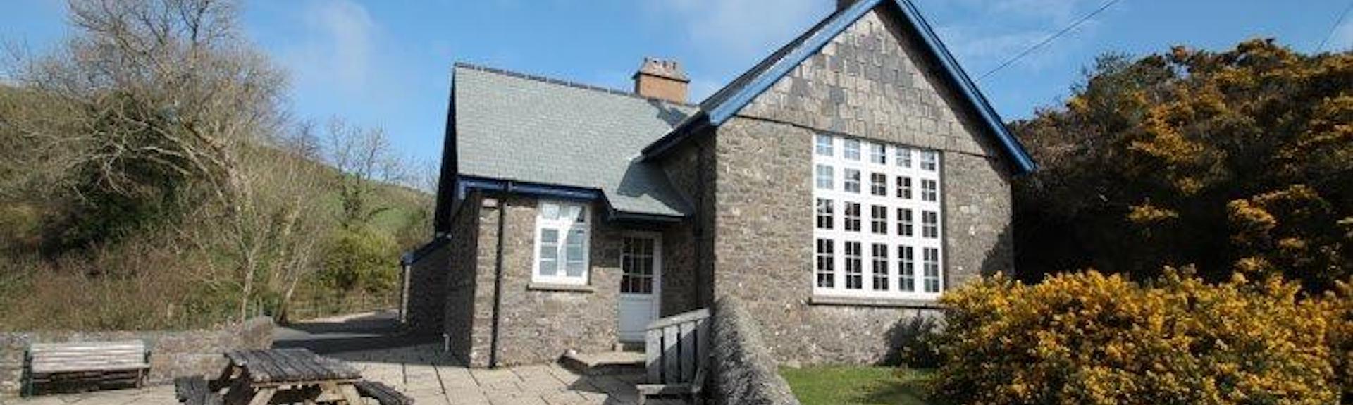 A converted stone-built school house with a lawn and large patio.