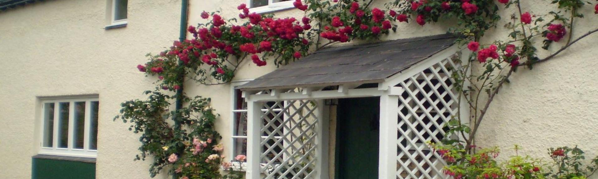 Climbing roses surround the porch of a country cottage in Somerset.