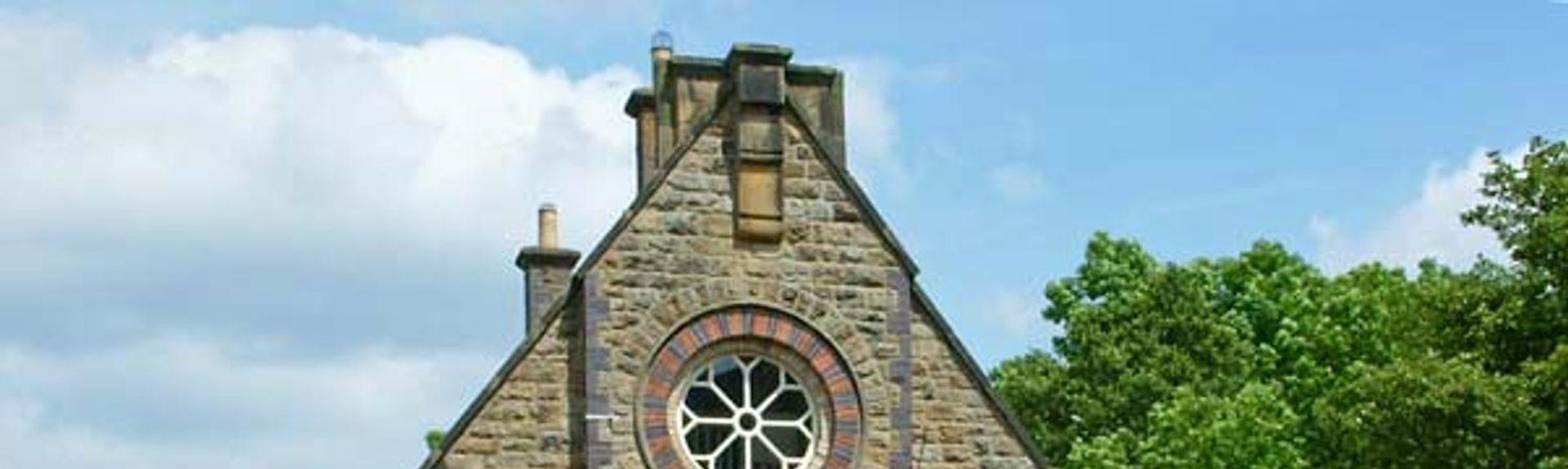 A chapel conversion with a large rose window sits behind a low stone wall.