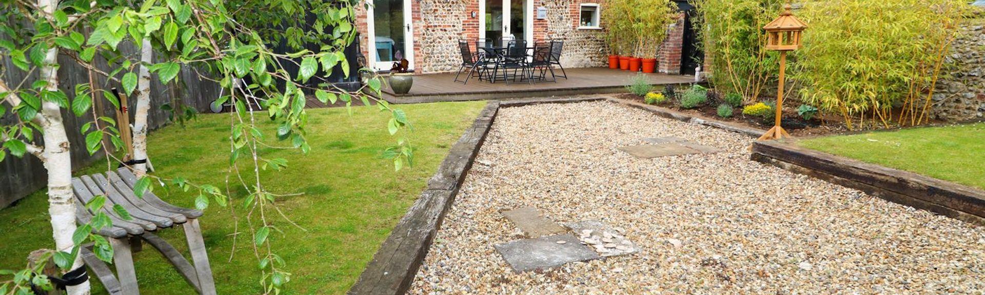 A shingle path leads up to a stone-built Norfolk bungalow with two long lawns.