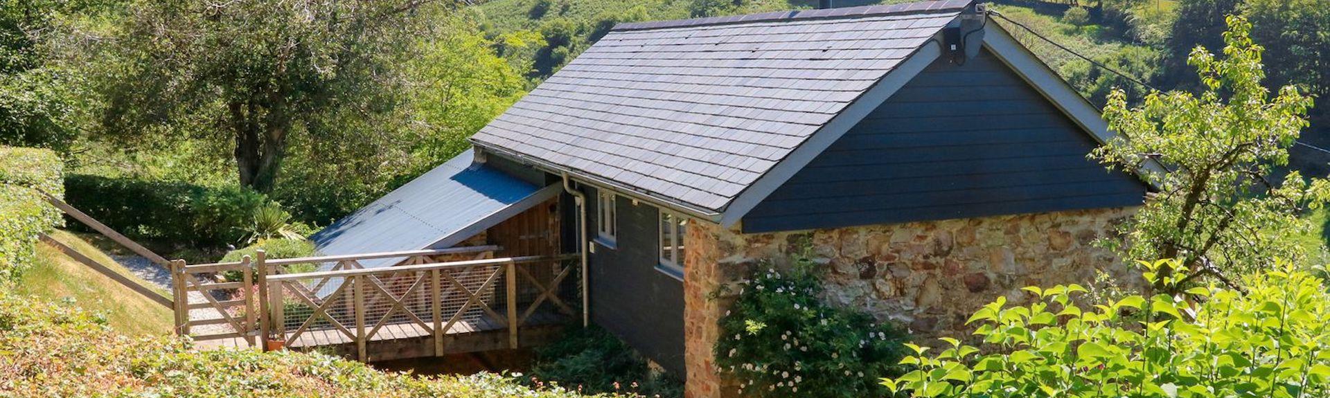 A single storey barn conversion in North Devon surrounded by gardens and tall hedge rows.
