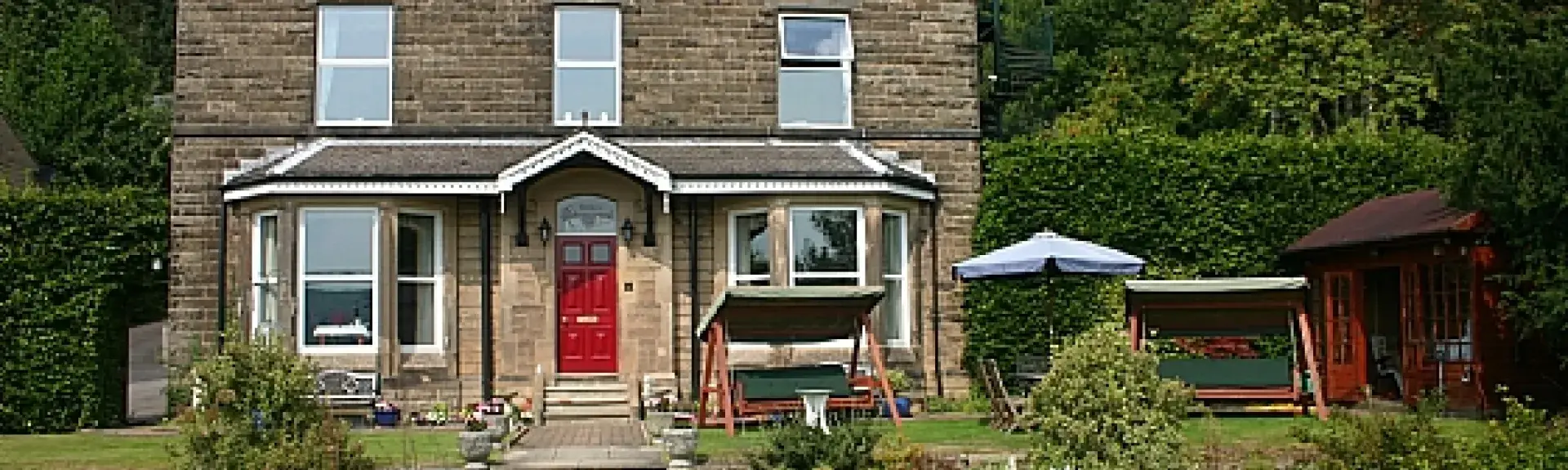 Exterior of a stone-built, 3-storey detached house  in front of a wood and overlooking a terraced garden
