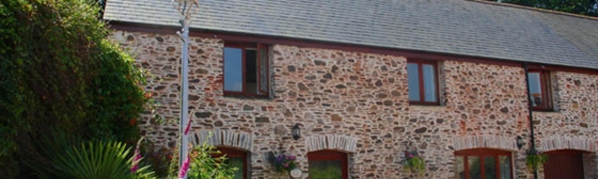 A stone-built, 2-storey courtyard cottage with foxgloves flowering in its garden.
