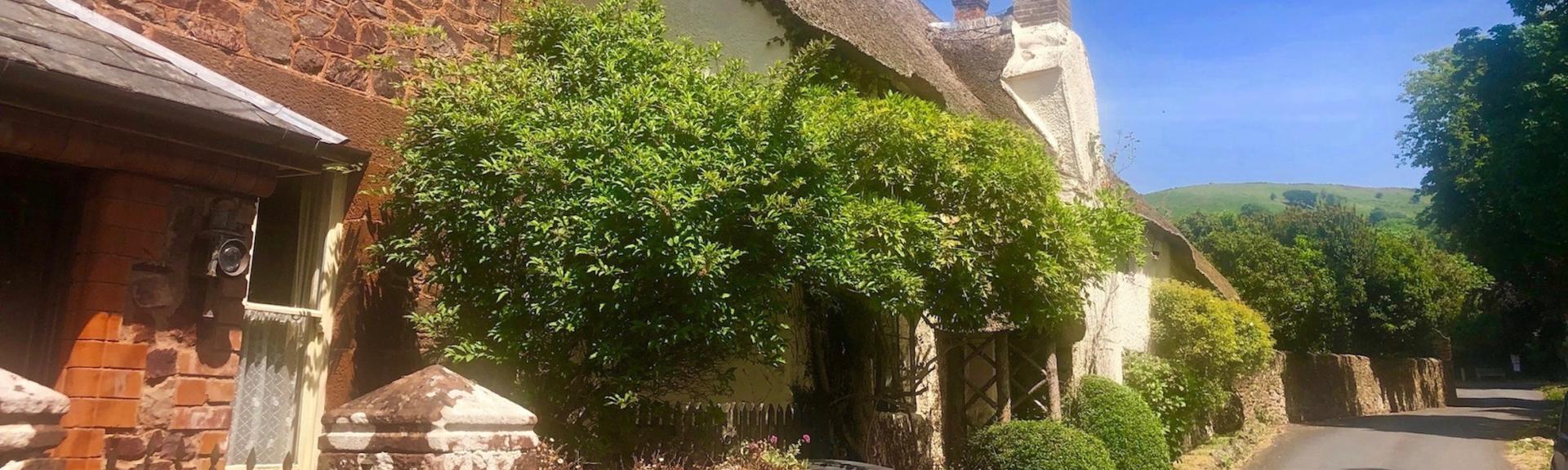 Wisteria-clad Quantock holiday cottages on a village street on a sunny day.