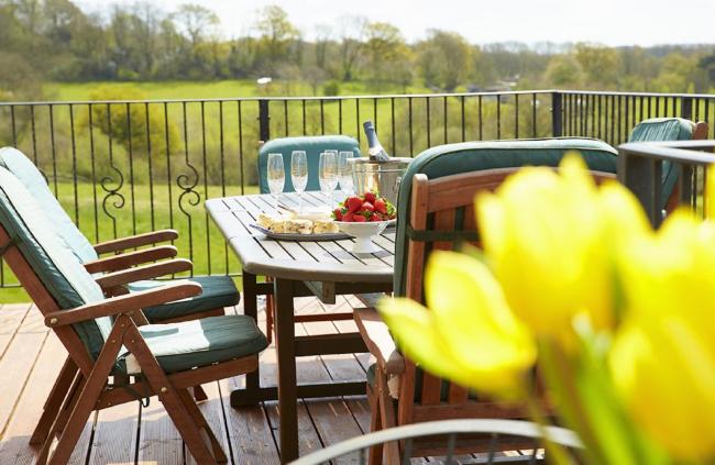 Outdoor Dining on the Deck at Underwood House in East Knoyle A dining table and chairs on a deck of a Wiltshire holiday cottage with fields in the background.