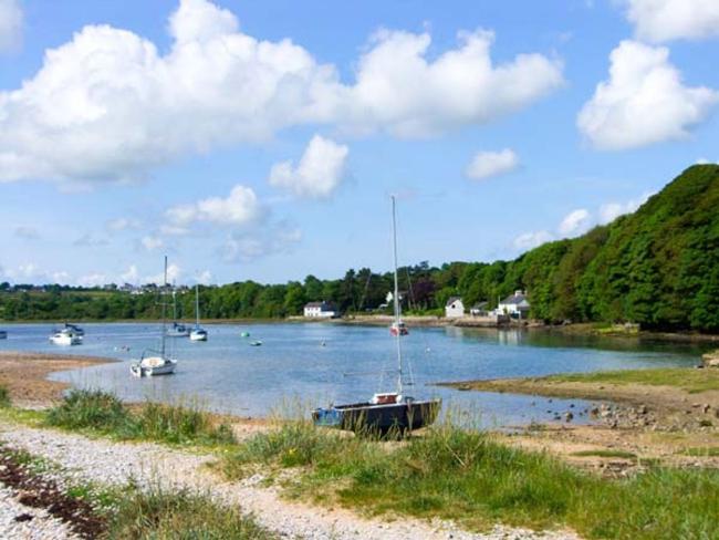 Photocredit: Awel-Mon Holiday Cottage, Anglesey. Benllech beach at low tide. A scttering of smallpleasure boat lie anchored in a bay. In the foreground is a small sandy beach. The far side of the bay is bordered by woods.