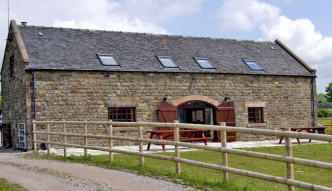 Botomouse Barn in Ipstones A long stone Yorrkshire Dales barn conversion with a slate roof and a set large oval-topped French windows in the centre. Outside is a patio with pinic banch anddining table overlooking a grassy lawn.