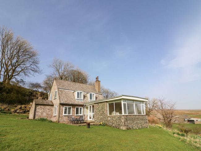 Netherscar Holiday Cottage in Iingleton A large stone-built house nestling into a tree-lined hillside. An extension to the house has wrap around windows to take advantage of moorland views across the Yorkshire Dales. A patio with pinic table and lawn surrounds the house.