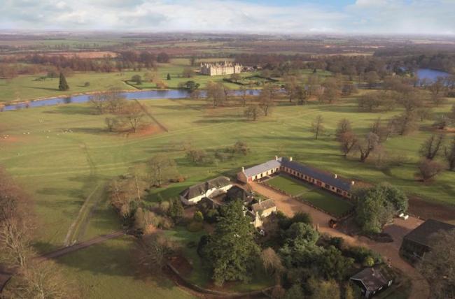 The Stables at Burghley - Luxury Lincolnshire Holiday Home. Aerial view of the flat Lincolnshire countryside dotted with houses and small farms. In the foreground is an impressive courtyare bulding, once stables and now holiday cottages.