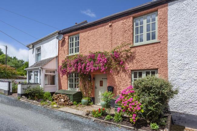 A double fronted terraaced cottage with a flower-clad creeper hanging above its front door.