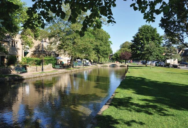 Waterside gardens in the heart of Bourton-on-the Water A calm stream flows through tree-lined waterside gardens overlooked by Cotswold cottages in Bourton-on-the-Water.