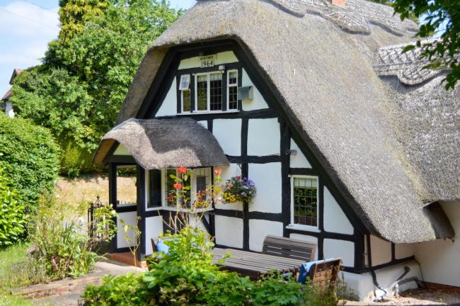 Corner Thatch Holiday Cottage in Alcester Gable end of a half-timbered thatched cottage with the roof reaching right to the ground.