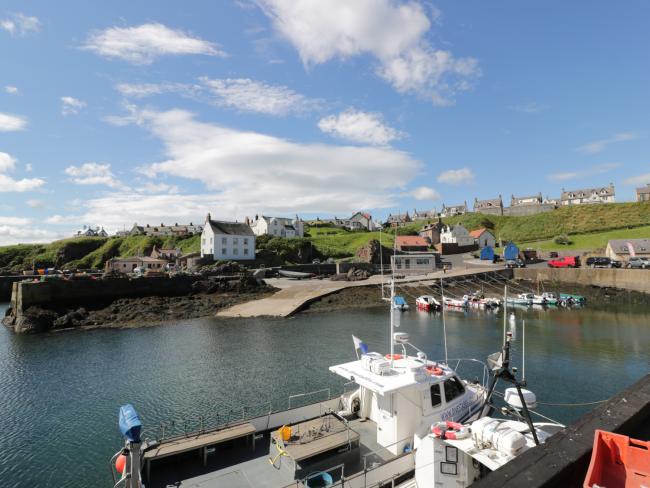 Find Waterside Holiday Cottages in St Abbs Small craft and fishing boats are moored to a quayside in St. Abbs, with village builldings in the backfround.