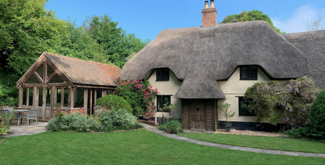 Under Acre Cottage i Blandford Forum A thatched holiday cottage in Blandford Forum with a slate-roofed extension overlooks a well-kept lawn