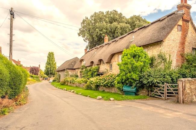 Escape to Amberley For a Peaceful Holiday in the West Sussex Countryside. A row of thatched cottages with flower-filled front gardens overlook an empty village street.