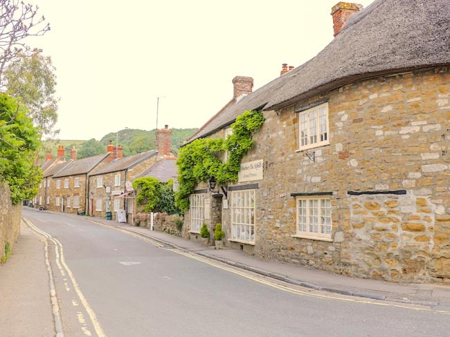 Abbotsbury's Historic High Street in Dorset. A villge street in Dorset lined by old ston-bult cottages with thatched roofs.