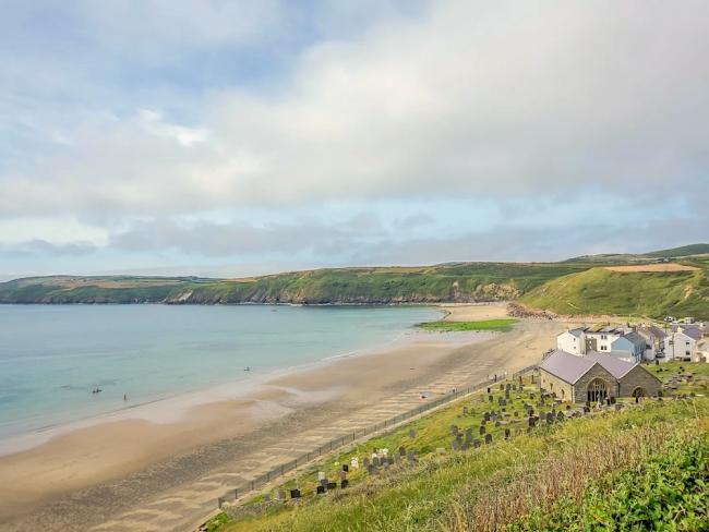 Image credit: Pen Y Bont Cottage in Aberdaron. A Welsh beach stretches around a wide bay backed by low hills.