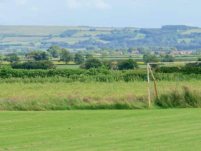 Discover Country Cottages in Allerston A view across fields to the rooftops of a small village beneath large hills.