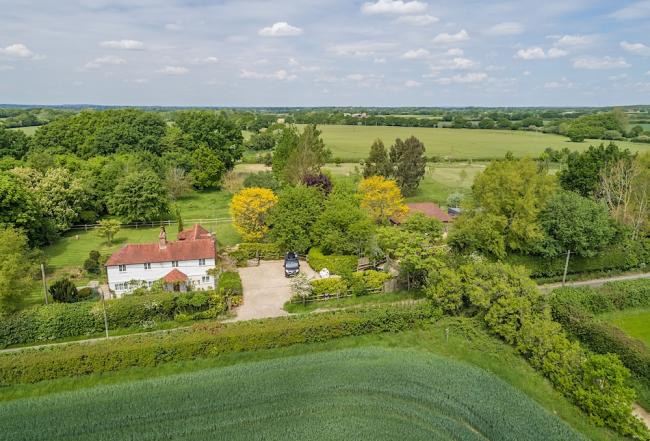 Cherry Tree Cottage Near Lewes An aerial view of woods and fields in high summer with a large tiled cottage overlooking a lane in the foreground.