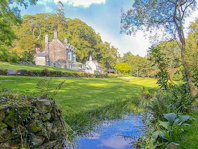 A large stone-built house stands above agrassy field that slopes down to a small river. near Dolgellau in Snowdonia..
