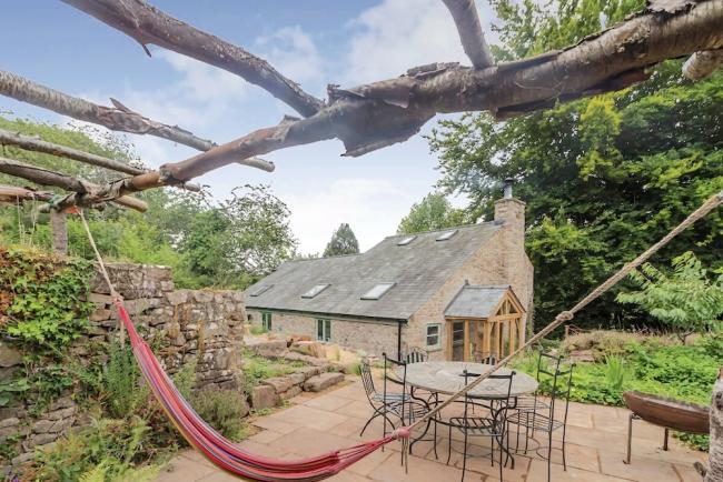 View Gloucestershire Holiday Cottages. Photo credit: Endless Esther in Hewelsfield he patio garden and exterior of a Gloucestershire holiday home with an outdoor dining table and a hammock strung between trees.
