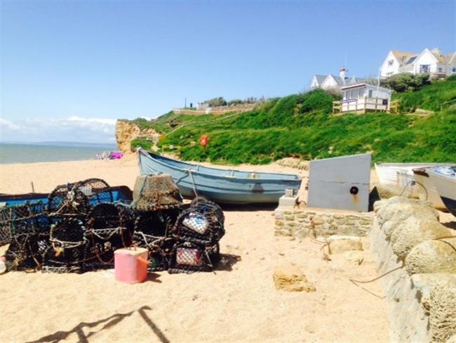 View Burton Bradstock Holiday Cottages A beach scene with small boats and lobster pots on the sand.