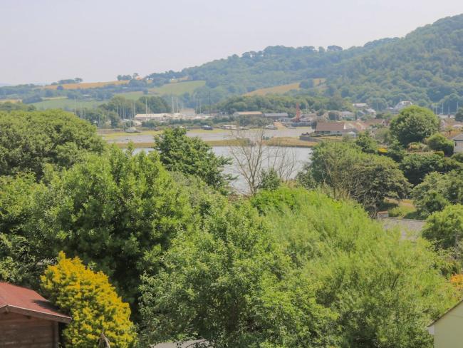 Coastal Holiday Cottages in Cawsand Beyond a cluster of trees lies a lake with its shores dotted with small buildings.