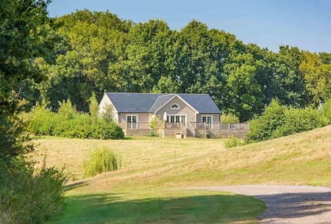View Essex Coast and Countryside Holiday Cottages A New England style wooden holiday lodge. In the foreground are sloping fields while behind the lodge is a wood.