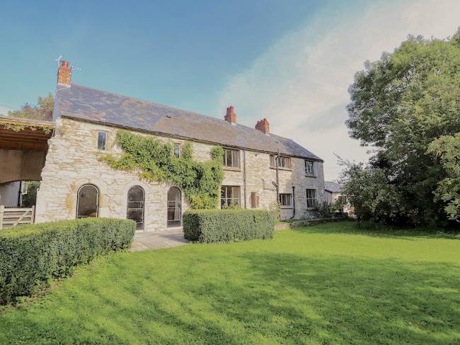 A long 2-storey stone-built cottage overlooks trees and a large lawn.