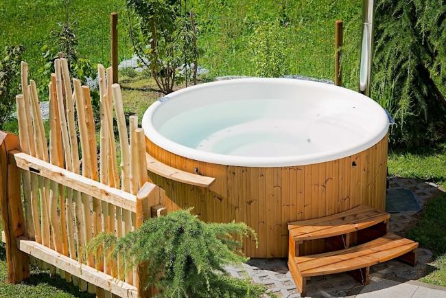 Find and Book A Cottage Holiday With a Hot Tub A wooden eco-friendly hot-tub on a deck surrounded by trees in summer.