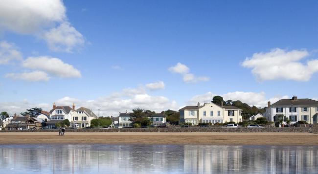 A row of detached house and cottages face a beach at high tide.