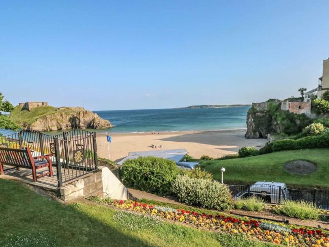 A  hillside garden with a terrace of flowers sloping down to a sandy cove.